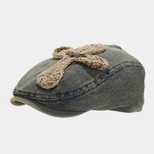 Detail of blue denim beret with khaki woven cross and metal accent in vintage style