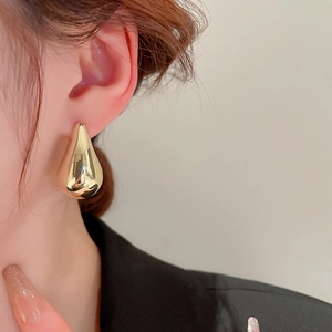 Macro side view of polished gold teardrop earrings showing the elegant drop on model