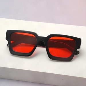 Detail view of bold black square frame sunglasses with vibrant red lenses on a white pedestal
