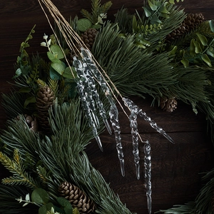 Transparent acrylic Christmas icicle ornaments hanging on pine needles with pine cones