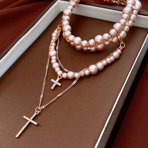 Macro shot of layered pink pearl necklace with gold cross pendants on jewelry tray