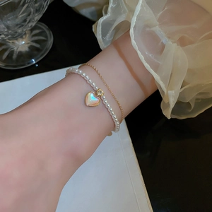 Close-up of double-layered gold bracelet with pearl beads and cat-eye heart charm