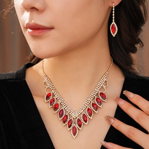 Close-up of elegant gold V-neck necklace and earrings with red gems and sparkling rhinestones
