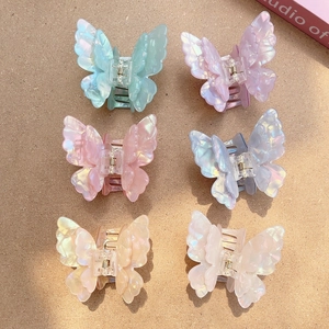 Detail of six iridescent butterfly hair claws in pastel shades on a textured surface