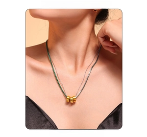 Detail of double-layer necklace with green gemstone and three golden cylinders on model