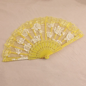 Détail d'éventail pliable en dentelle jaune avec motifs de roses blanches et paillettes