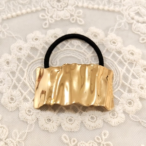 Detail of a wavy gold metal accent on a black elastic hair tie over white lace fabric