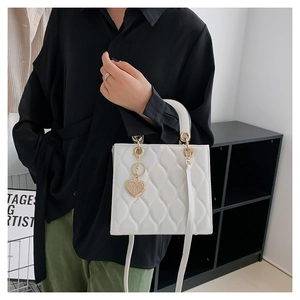 Detailed side view of white quilted leather bag with golden heart charm and strap