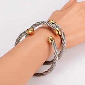 Two-tone stainless steel cable wire cuff bracelet with gold bead accents on hand model