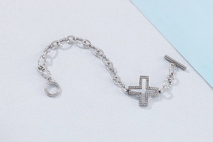 Detail of silver twisted chain bracelet featuring a hollow cross pendant and OT toggle clasp