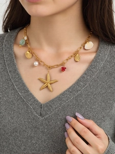 Golden ocean necklace with starfish, shells and pearls worn by a model on a grey sweater