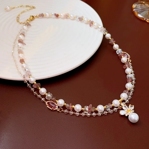 Detail of layered gold necklace with white pearls, pink stones, and a bow pendant