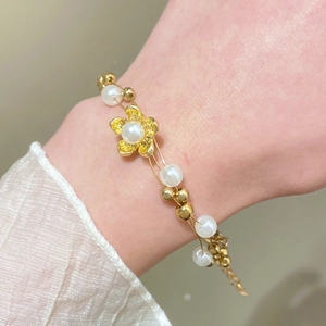 Primer plano de una pulsera dorada de doble hilera con flores y perlas en la muñeca