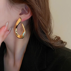 Detail showing irregular twisted gold metal earring with a fluid liquid metal texture