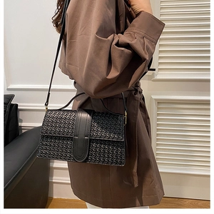 Close-up of black woven texture shoulder bag worn by model with brown trench coat