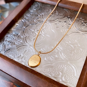 Golden titanium steel snake chain with engraved oval pendant on vintage tray