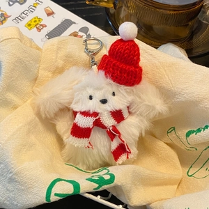 Close-up of a plush white puppy keychain wearing a red knit hat and striped scarf