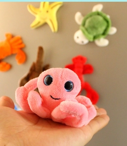 Close-up of a small pink plush octopus magnet held in hand with ocean themed background