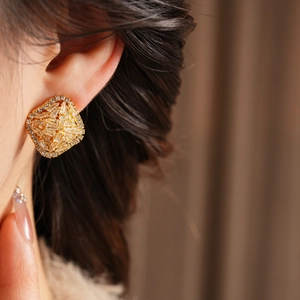 Close-up of elegant gold square earrings with inlaid zircon on a female model