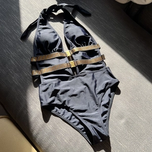 Sultry black halter one-piece swimsuit featuring gold-striped waist bands and buckle accents