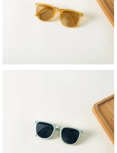 Close-up of foldable kids sunglasses in amber and mint green frames on wooden tray