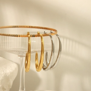 Detail of gold and silver hollow C-shaped earrings on textured glass with polished finish