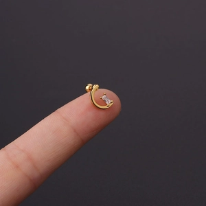 Macro shot of gold tragus stud with zircon on fingertip showing its mini size