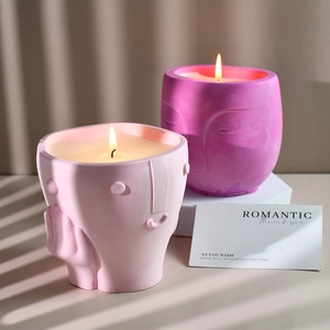 Detailed view of pink ceramic candle cups with embossed face sculptures and lit flames