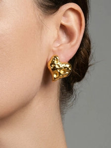 Makro-Detail des herzförmigen Ohrrings in Gold mit gehämmerter Metalloberfläche Optik