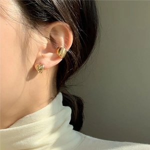 Close-up of a gold heart-shaped earring and a wide ear cuff on a model's ear