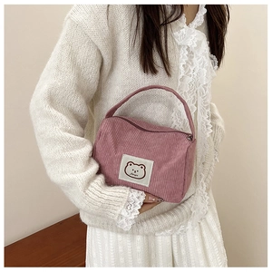 Pink corduroy handbag featuring a cute cartoon bear patch held by a model in a white top