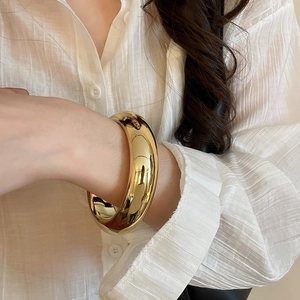 Close-up of a wide polished gold bangle on a white shirt sleeve featuring mirror finish