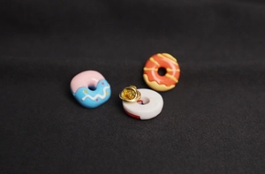 Detailed view of three cute 3D donut enamel pins with golden butterfly clasp closures