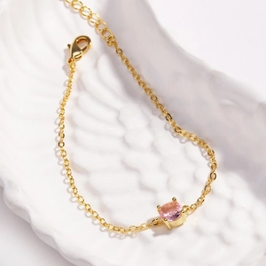 Close-up of a gold chain bracelet featuring a round pink stone on a white ceramic surface
