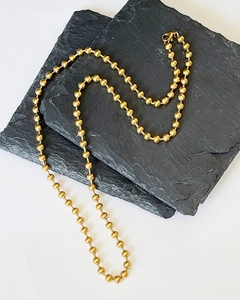 Detail of minimalist gold bead chain necklace with lobster clasp on grey slate