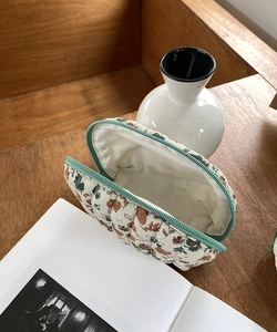 Quilted floral cosmetic bag with mint green zipper shown open on a wooden table