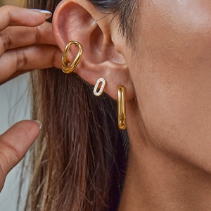 Detailed view of layered gold ear cuff, zircon stud, and hoop earring on a model