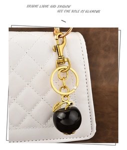 Detail of a black apple keychain with gold metal hardware on a white quilted handbag
