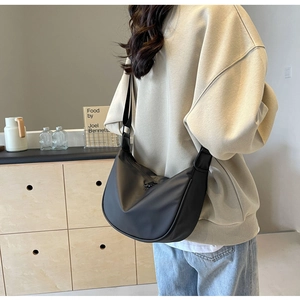 Detailed side view of black crossbody dumpling bag with wide strap on a model