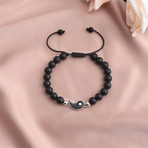 Dettaglio del bracciale con perline nere opache e ciondolo Yin Yang su fondo di seta