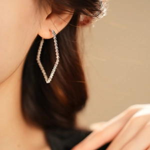 Close-up of silver rhombic geometric hoop earrings with textured finish worn by a model