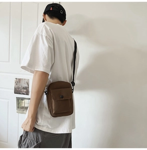 Detail of a dark brown mini crossbody bag with snap closure and adjustable strap