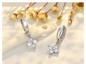 Makroaufnahme von Kleeblatt-Ohrringen aus Silber mit Zirkonia auf getrockneten Blumen