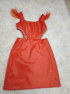 Détail d'une robe orange en similicuir avec plumes aux épaules et découpe à la taille