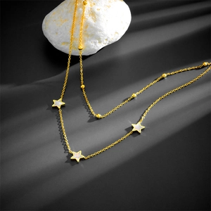 Double-layered gold necklace with star-shaped white shell pendants on stone surface