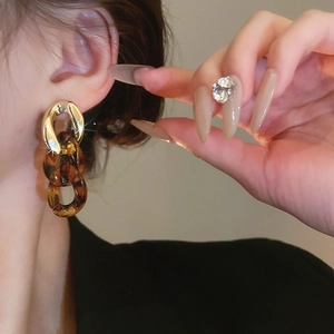 Close-up of leopard resin hoops and gold metal interlocking earrings on a model