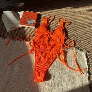 Dettaglio del costume da bagno intero arancione testurizzato con lacci laterali e coulisse