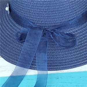 Detailed close-up of blue straw hat featuring an organza bow and pearl accent