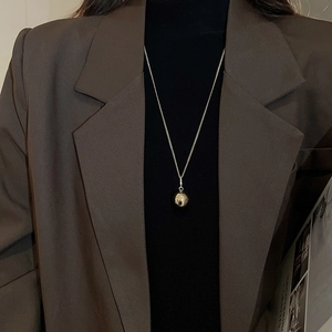Close-up of minimalist silver ball pendant necklace styled on a dark chic blazer