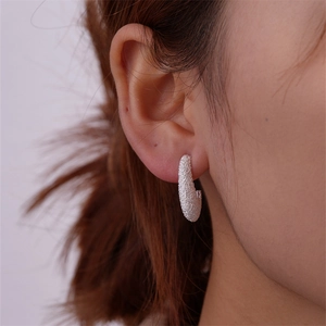 Macro detail of silver C-shaped frosted earrings on a model with shimmering texture